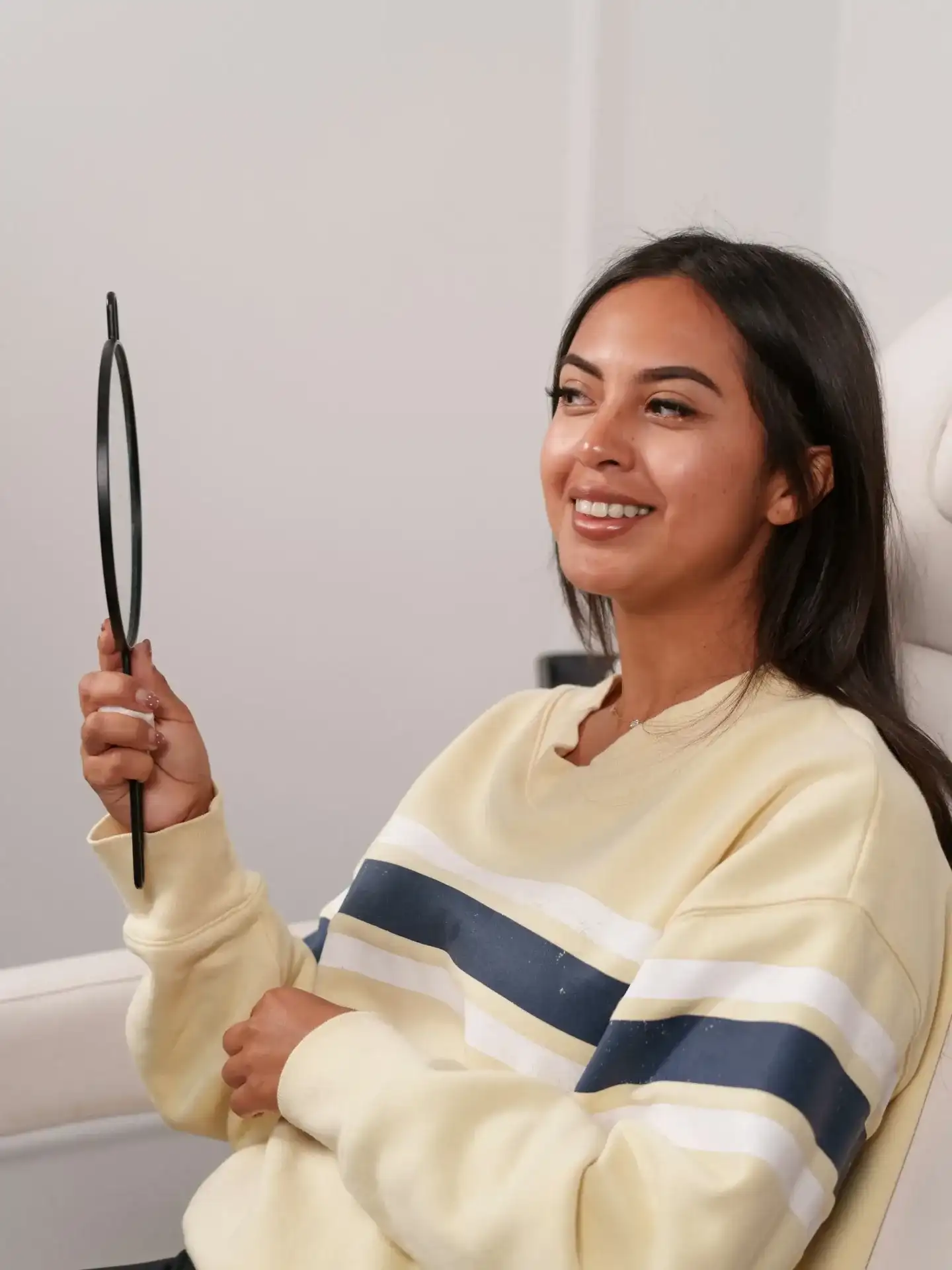 A client holding a hand mirror while seated in a clinic treatment chair