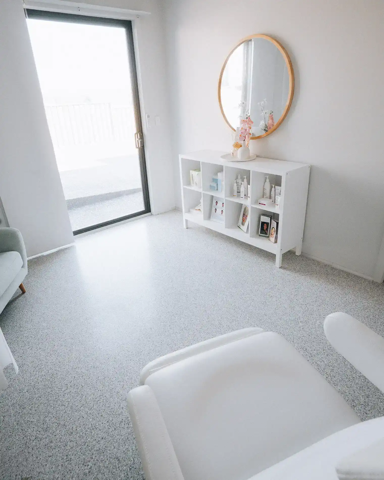 The clinic room at Wangi Wangi, with a sliding glass door opening onto the deck and a skincare console under a round timber mirror