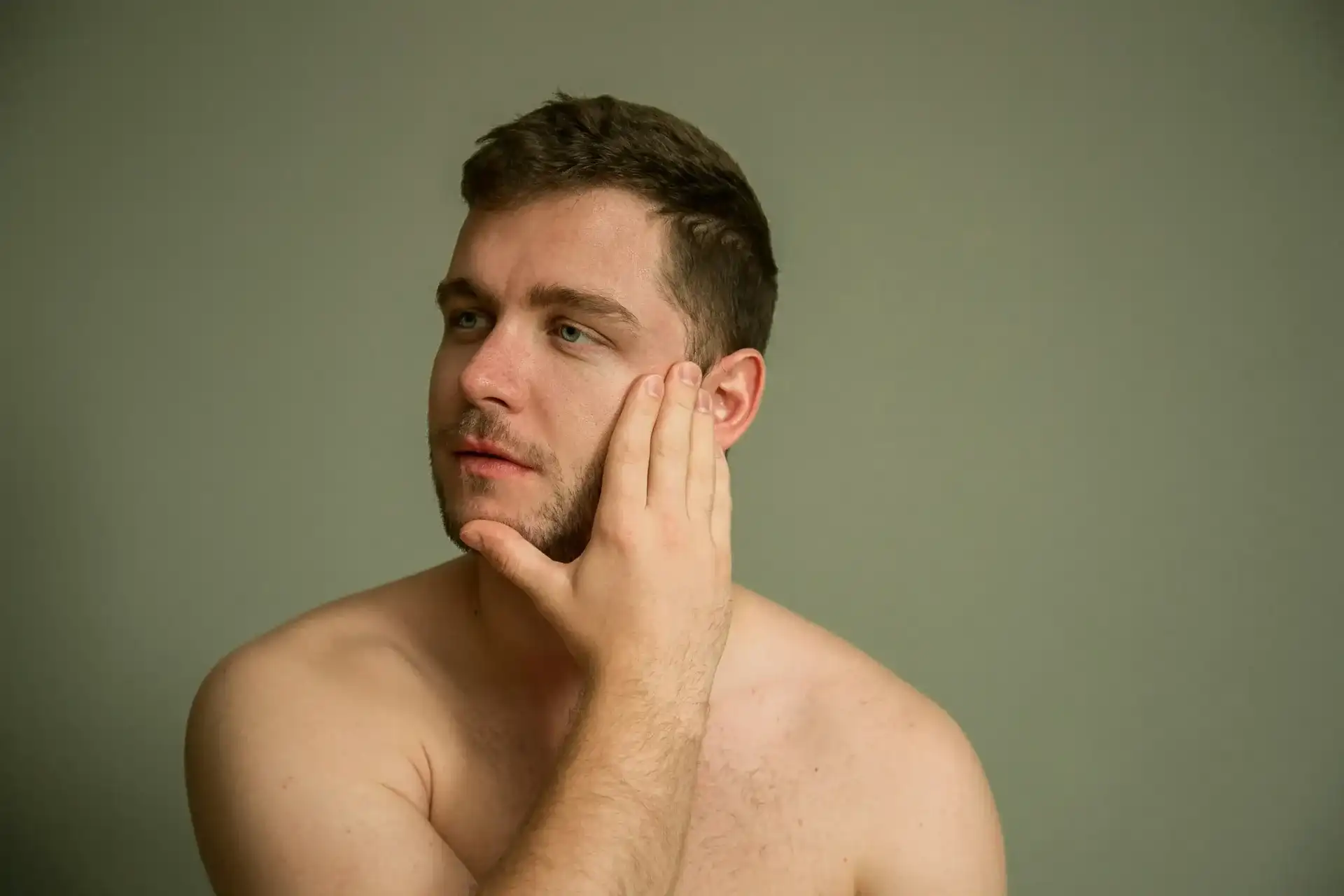 A man resting a hand against his jaw, considering the skin along his beard line