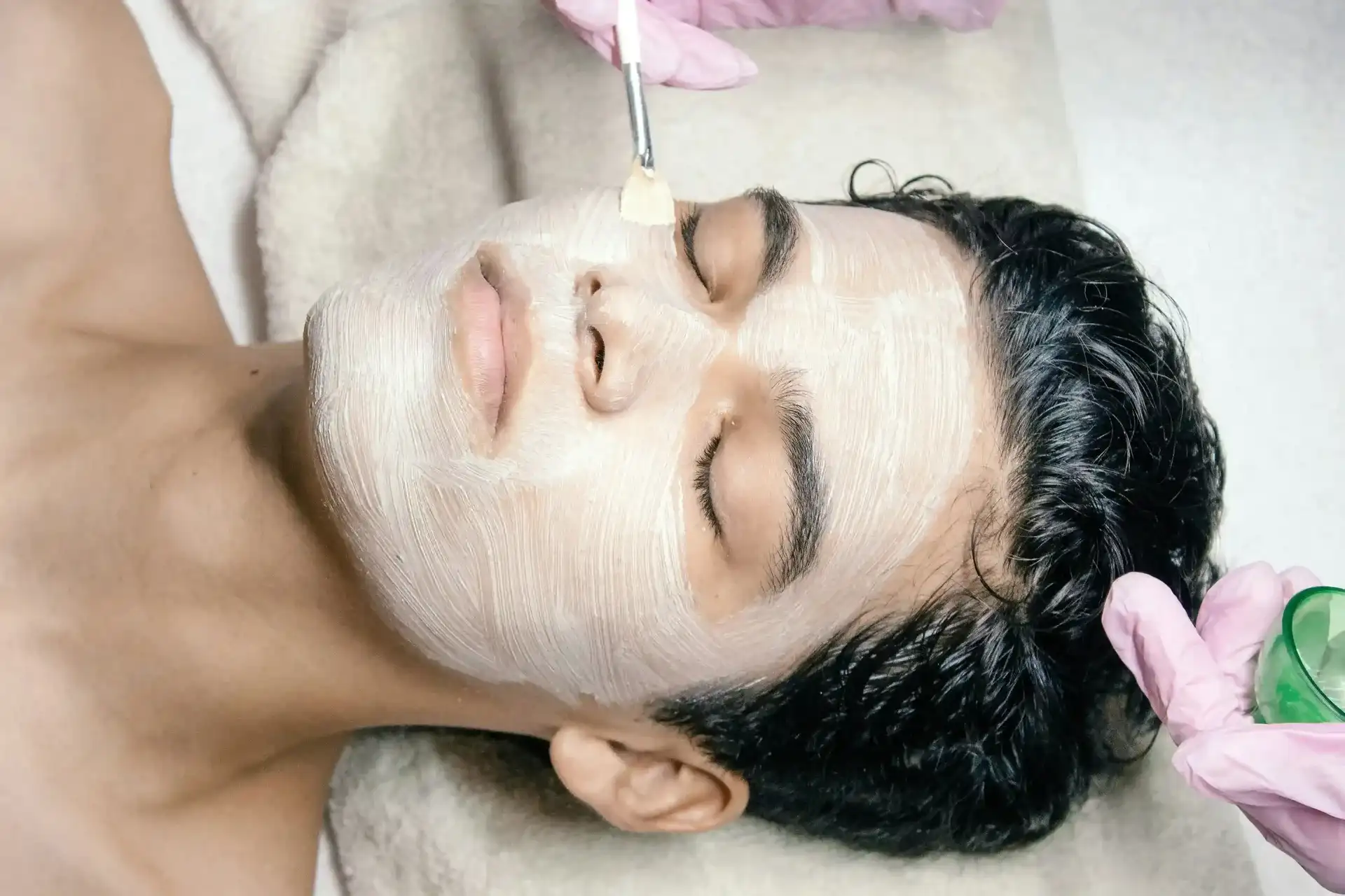 A practitioner applying a treatment mask across a man's face with a brush
